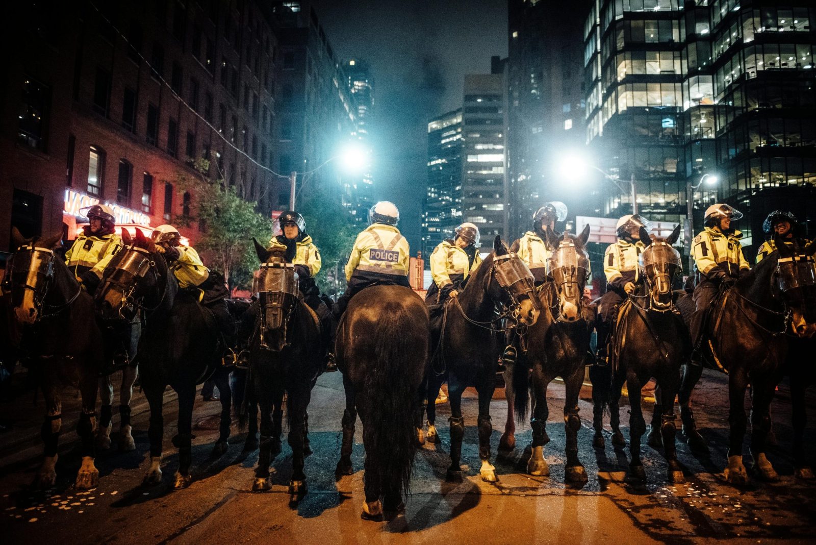 A line of mounted police officers in a city during a nighttime protest, maintaining order.